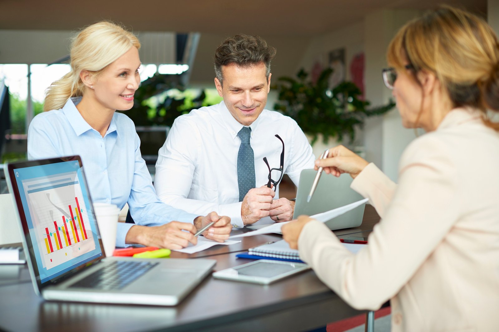 A group of professionals engage in a meeting, analysing data from a laptop and discussing documents around a conference table.
