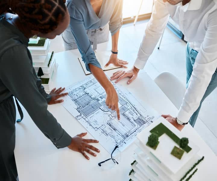 Three professionals architects discuss architectural plans, emphasising details with blueprints.
