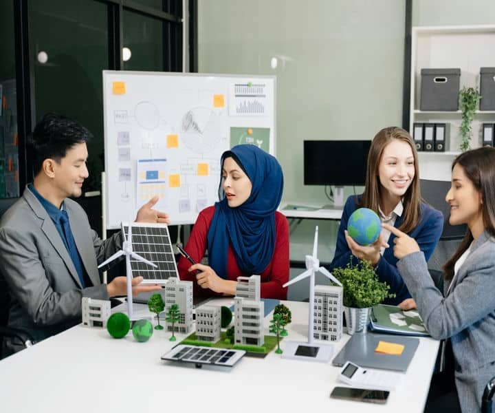 A group of professionals engaged in a discussion about sustainable energy, with model buildings, wind turbines, and solar panels on the table.