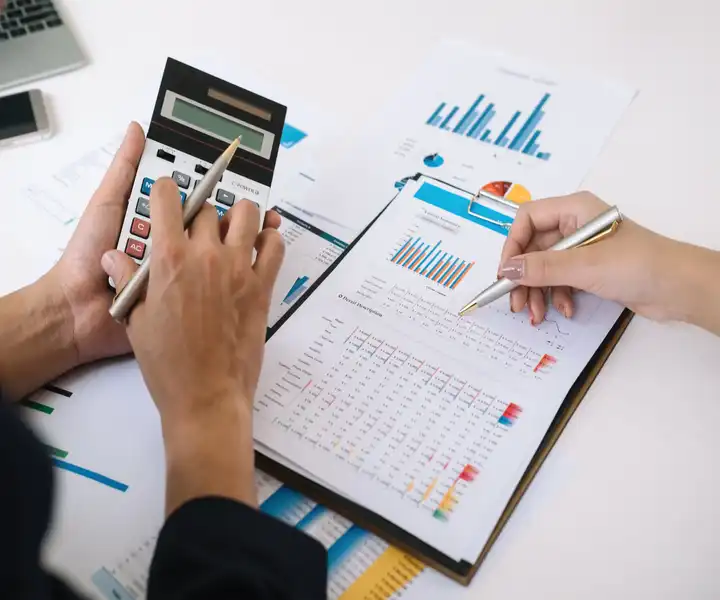 Two hands analyse data with a calculator and documents featuring colorful graphs and charts, indicating a business discussion.