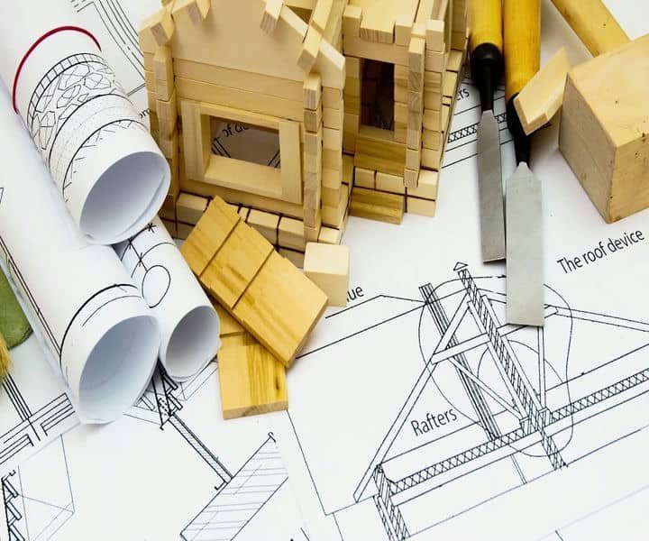 Wooden model houses and architectural blueprints surrounded by tools and construction materials, showcasing a building project.