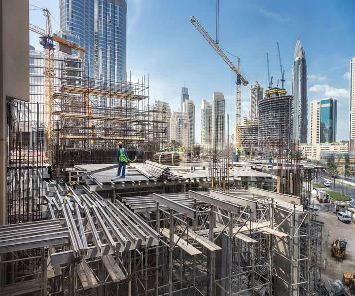 Construction site with a worker in safety gear, framed by skyscrapers and cranes.