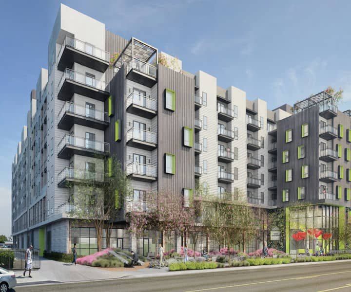 Modern multi-story apartment building with balconies, green accents, and landscaped surroundings in a sunny urban setting.