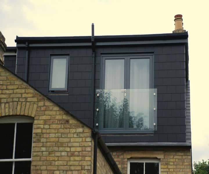 Modern dormer loft conversion with large windows, a glass balcony, and dark exterior cladding, featuring a brick lower wall.