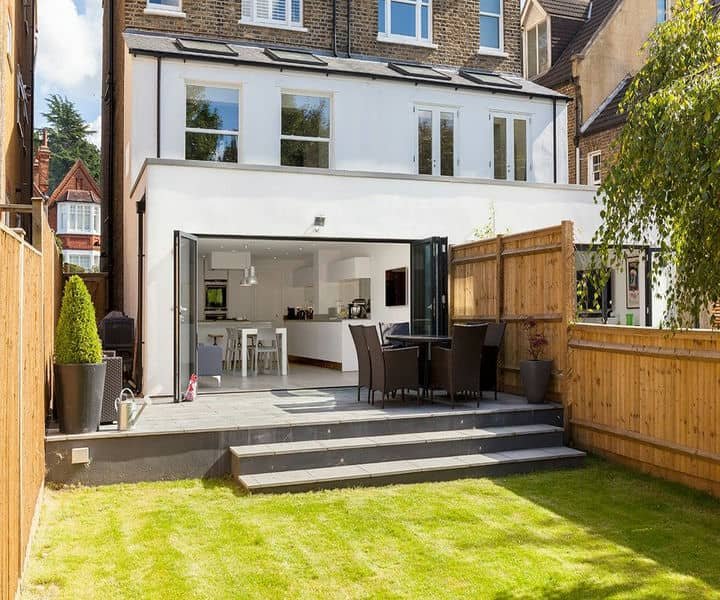 Modern double storey home extension with a large garden, and patio dining area, featuring open doors leading to a bright kitchen.
