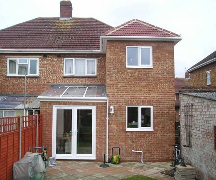 A two-story rear house extension with a southern-facing patio, featuring a glass door entrance and multiple windows, surrounded by a fenced yard.