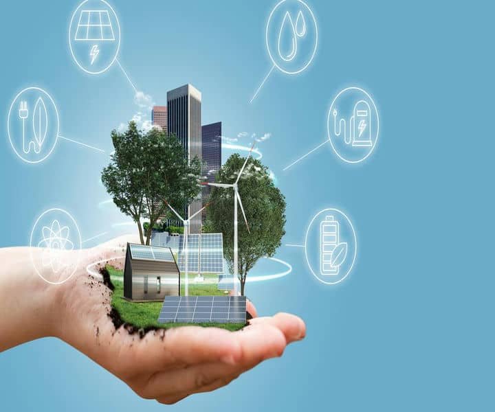 A hand holds a miniature eco-city with solar panels, wind turbines, and trees, symbolising sustainable energy and technology.