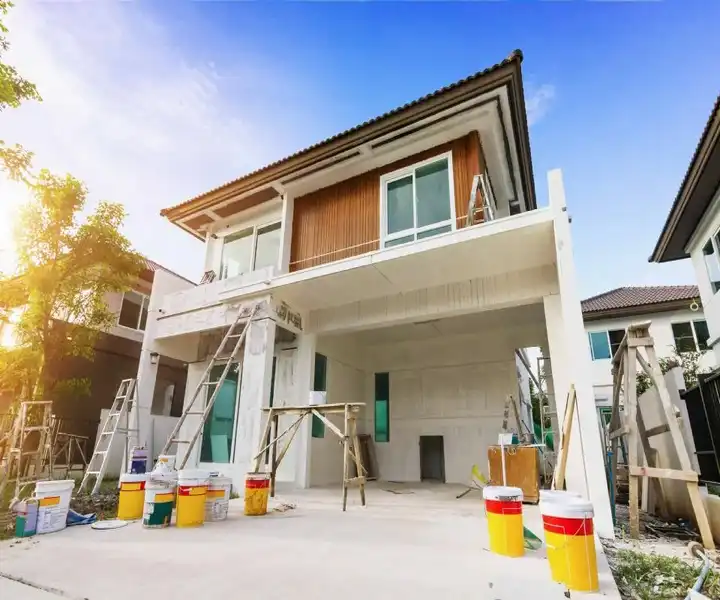 A modern house under construction, featuring scaffolding, paint buckets, and a clear blue sky in the background.