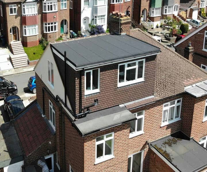A residential building featuring a modern flat roof, surrounded by brick houses and parked cars on a quiet street.