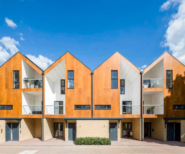 Modern houses with orange and white exteriors, featuring angular roofs and glass balconies against a blue sky and scattered clouds.