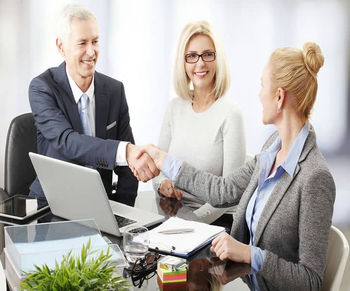 Two professionals shake hands across a conference table indicating a business consultation.