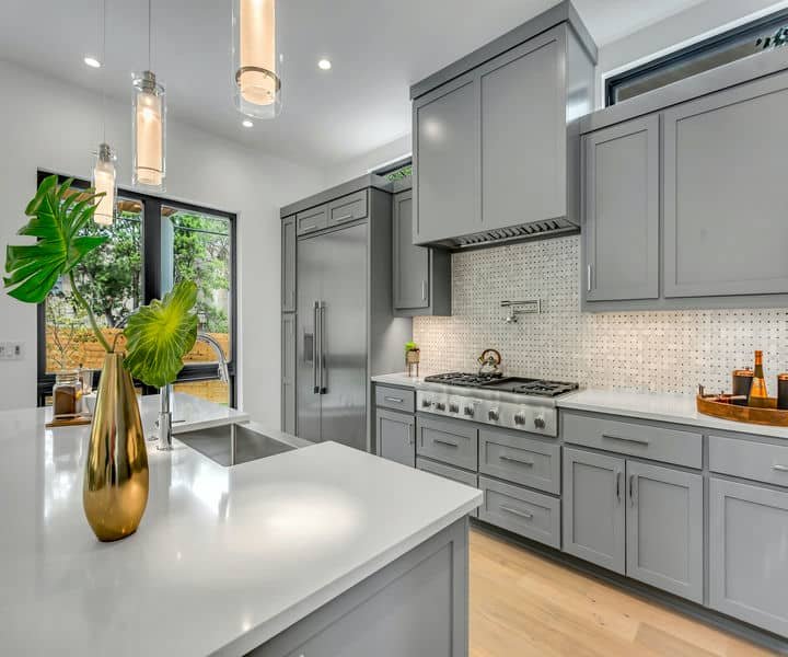 A well designed Modern kitchen with gray cabinets, appliances, and a bright window with greenery. Also Featured a white island.