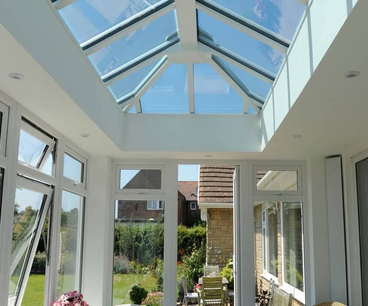Bright conservatory with glass ceiling and large windows, showcasing a garden view and modern furniture.