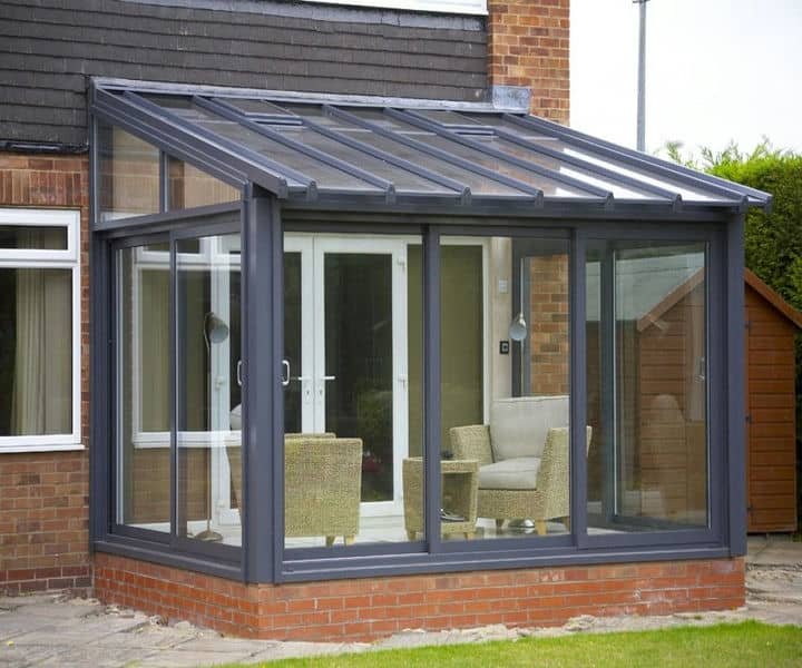 Modern lean to glass conservatory attached to a brick house, featuring two wicker chairs and large glass doors.