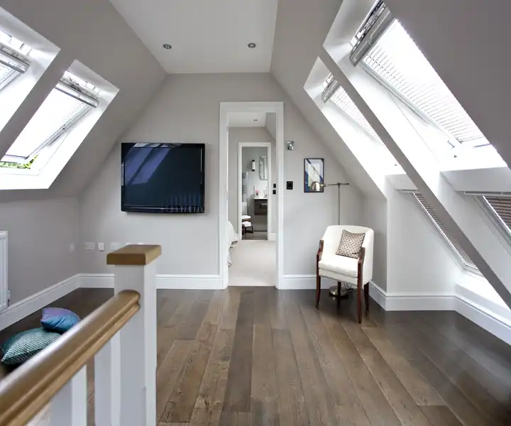 Bright and modern attic living space featuring angled skylights, dark wood flooring, and a wall-mounted TV.