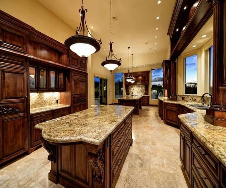 Luxurious kitchen with dark wooden cabinets, elegant lighting, and spacious granite countertops, filled with warm, inviting light.