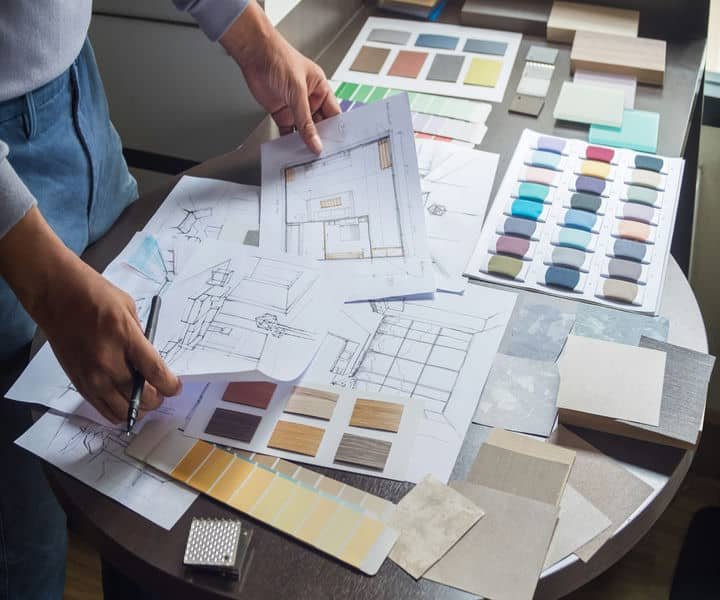 A designer reviews architectural sketches and fabric swatches on a table, planning interior materials and color palettes.