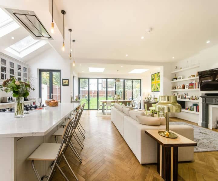 Modern open-plan living space with a quartz kitchen island, stylish seating, and large windows overlooking a green garden.