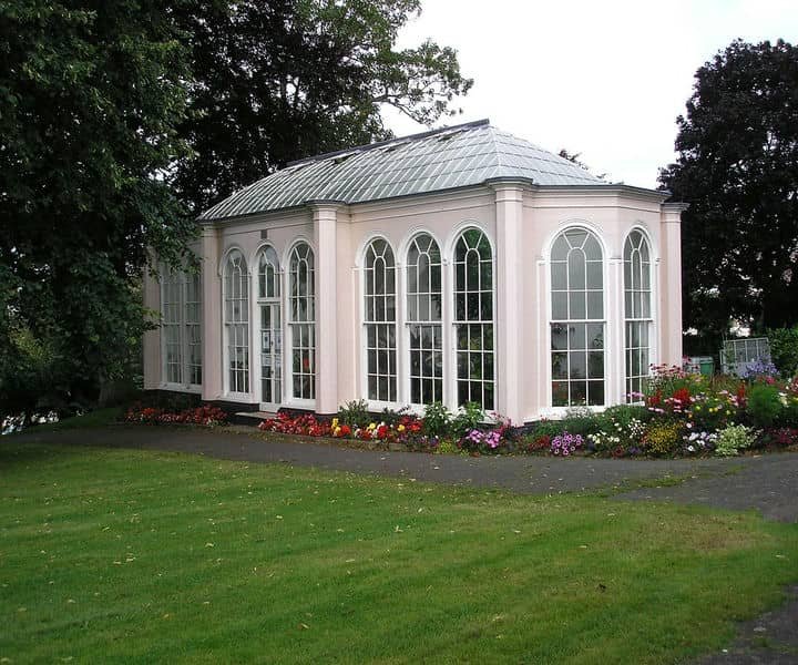 An orangery with arched windows, surrounded by colorful flowers and green grass.