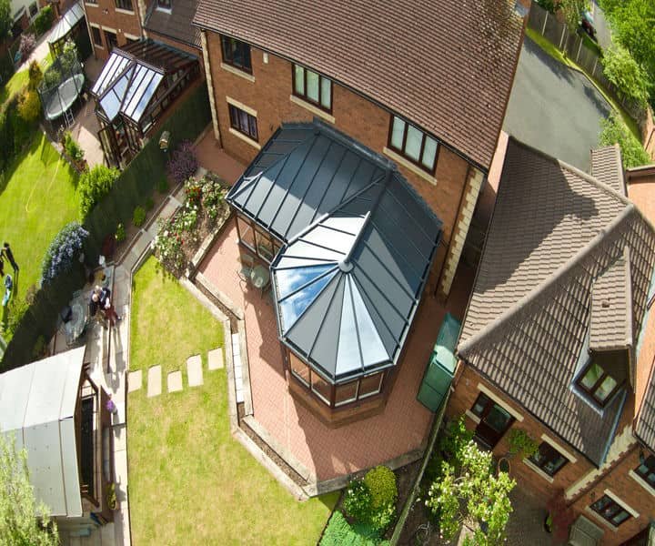 view of two brick houses with an elegant glass conservatory, surrounded by landscaped gardens and a patio area.