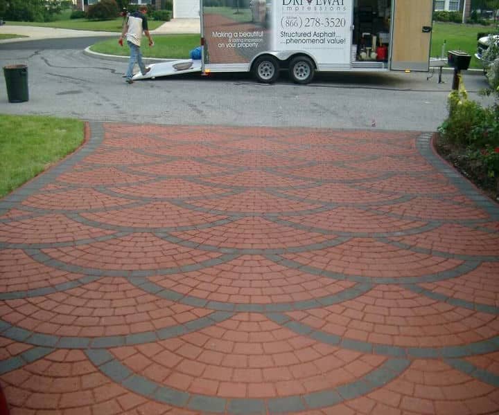 A patterned red brick driveway curves toward a trailer, showcasing a dropped kerb service.