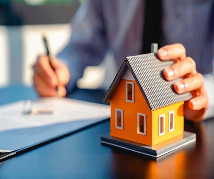 A businessperson with some document and a miniature orange house on the desk, symbolising real estate or home ownership.