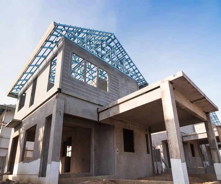 A partially constructed house with a visible blue metal roof frame and concrete walls.