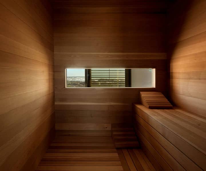 Interior of a wooden sauna featuring bench seating, smooth wooden walls, and a window allowing natural light and a view outside.