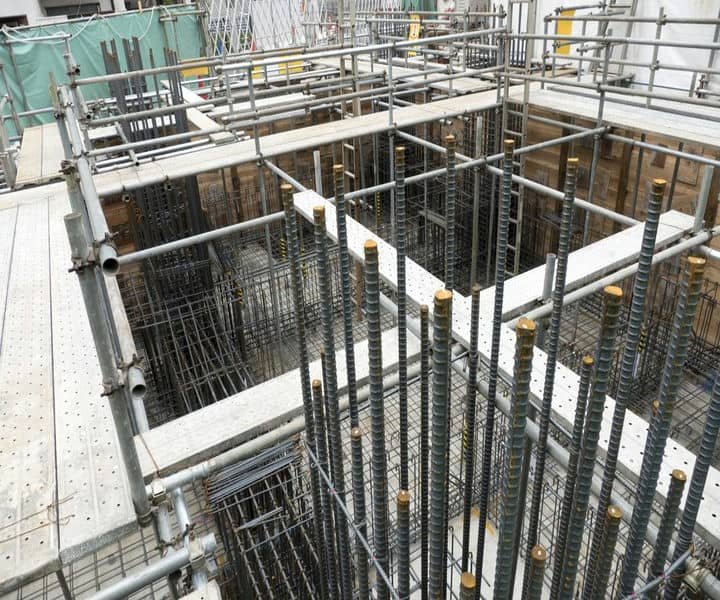 A construction site featuring a deep foundation with exposed reinforcing bars, scaffolding, and wooden forms for pouring concrete structures.