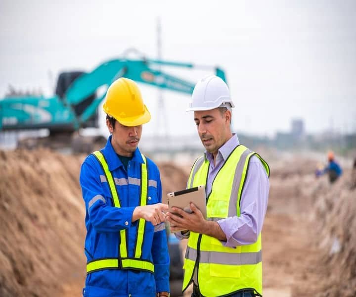 The surveyors are discussing plans on a site, with machinery.