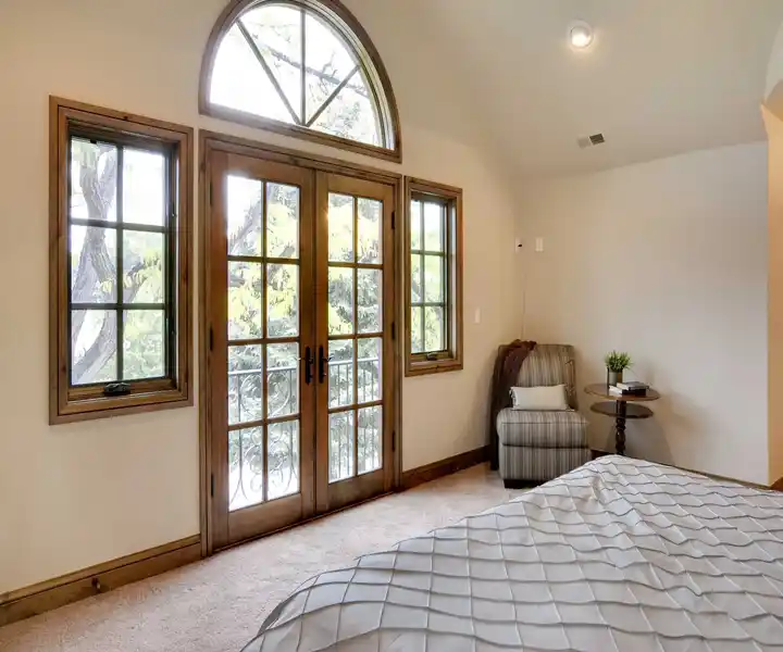 A cosy bedroom featuring a bed, large windows with French doors.