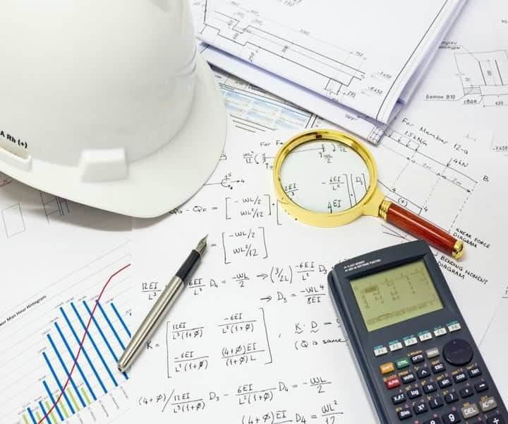 Engineering plans filled with calculations scattered on the table with other related equipments scattered.