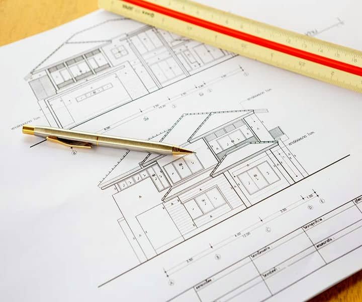 A pen rests on architectural blueprints, displaying detailed house designs and measurements, alongside a ruler for precision.