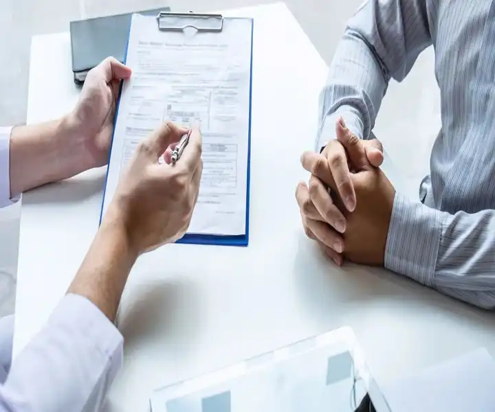 A person in a white coat holds documents discussing with a client.