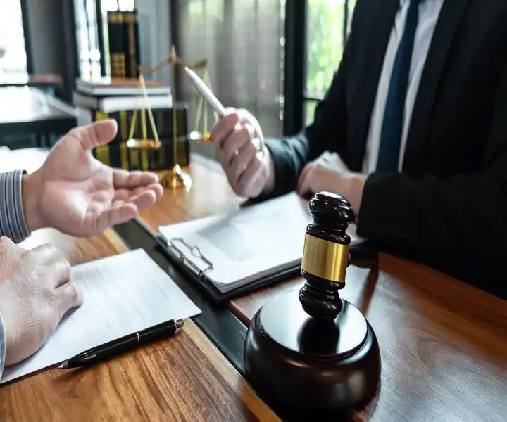 A close-up of a lawyer's desk with a gavel, legal documents, and hands gesturing during a consultation.